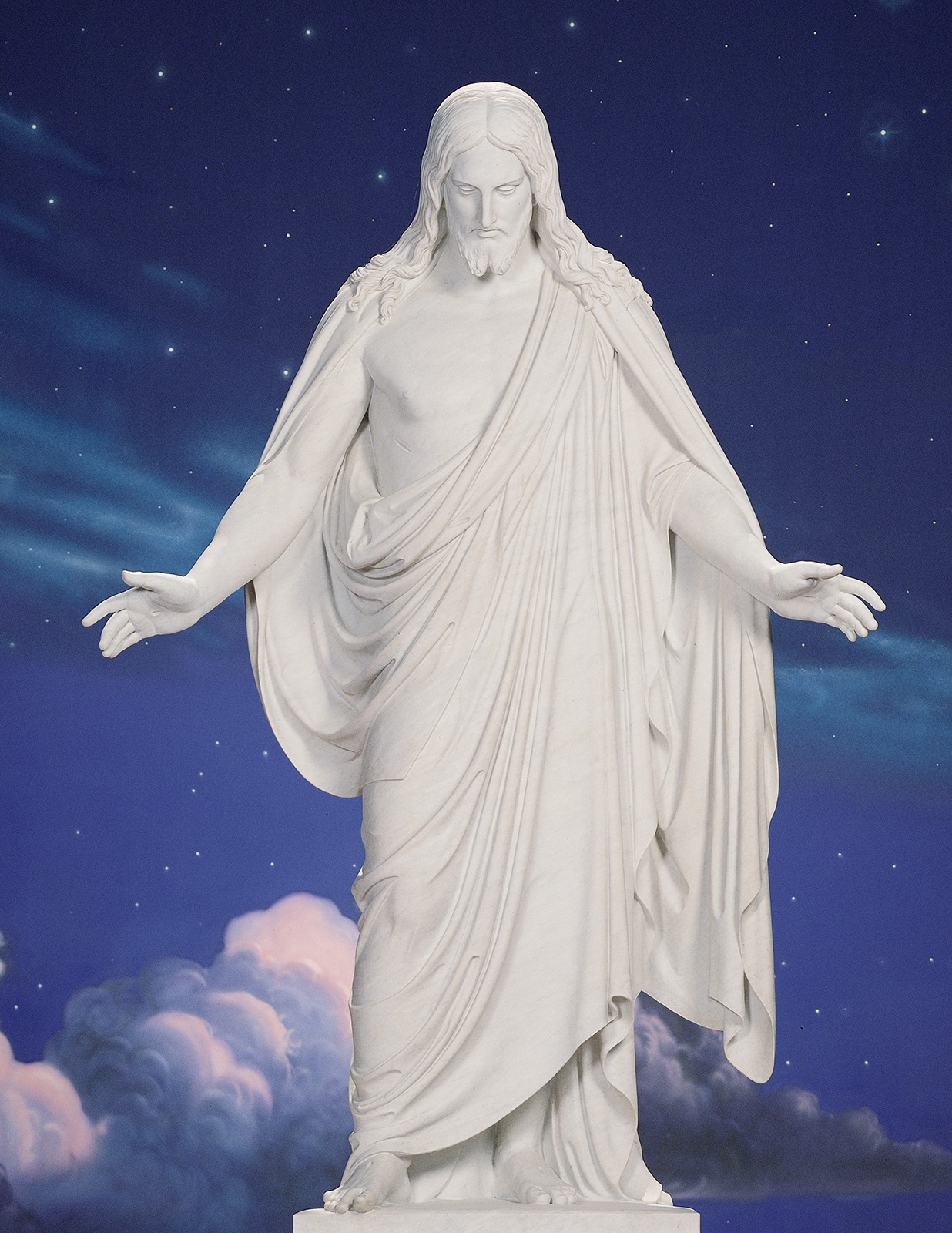 The Christus statue of Jesus Christ with outstretched arms against a star-filled blue background
